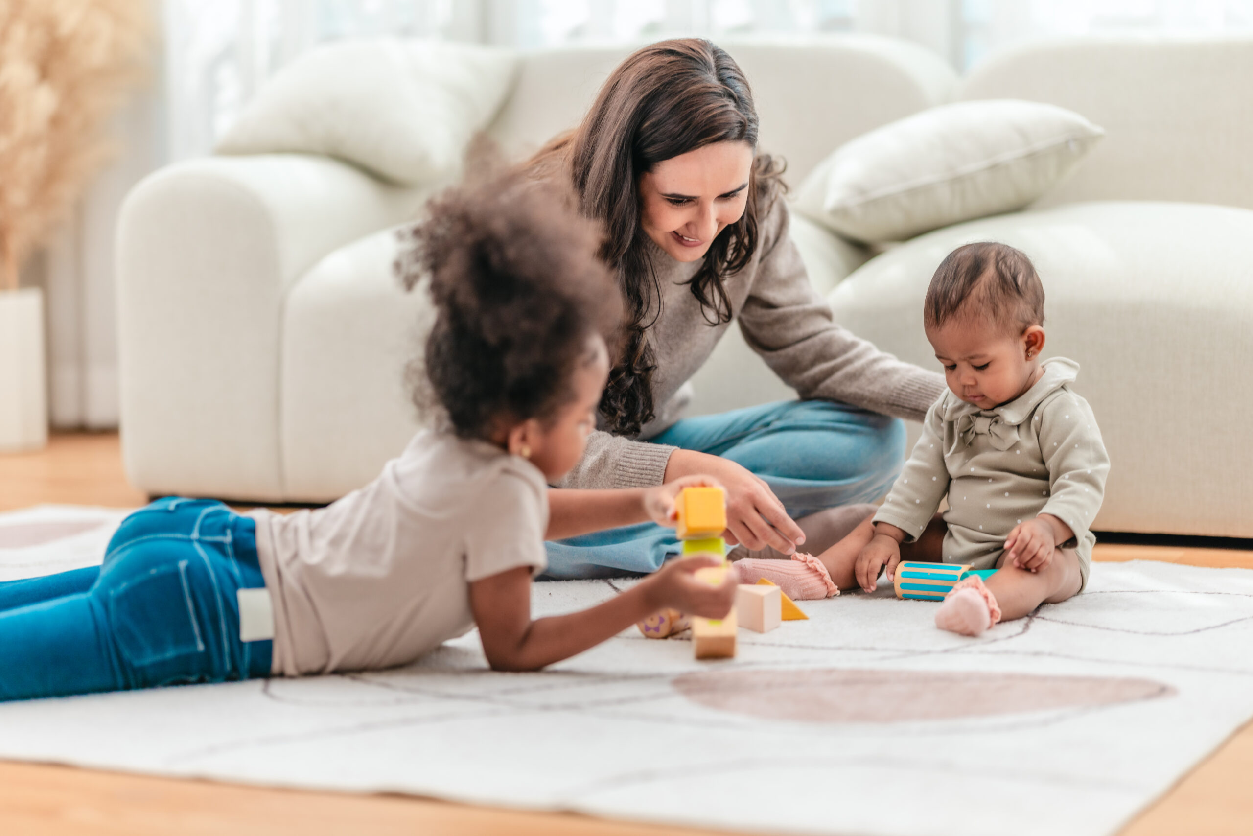 A joyful mother, playing and laughing with her two young daughters. The scene captures a warm, loving family moment with toys scattered around, highlighting early childhood interaction and bonding.